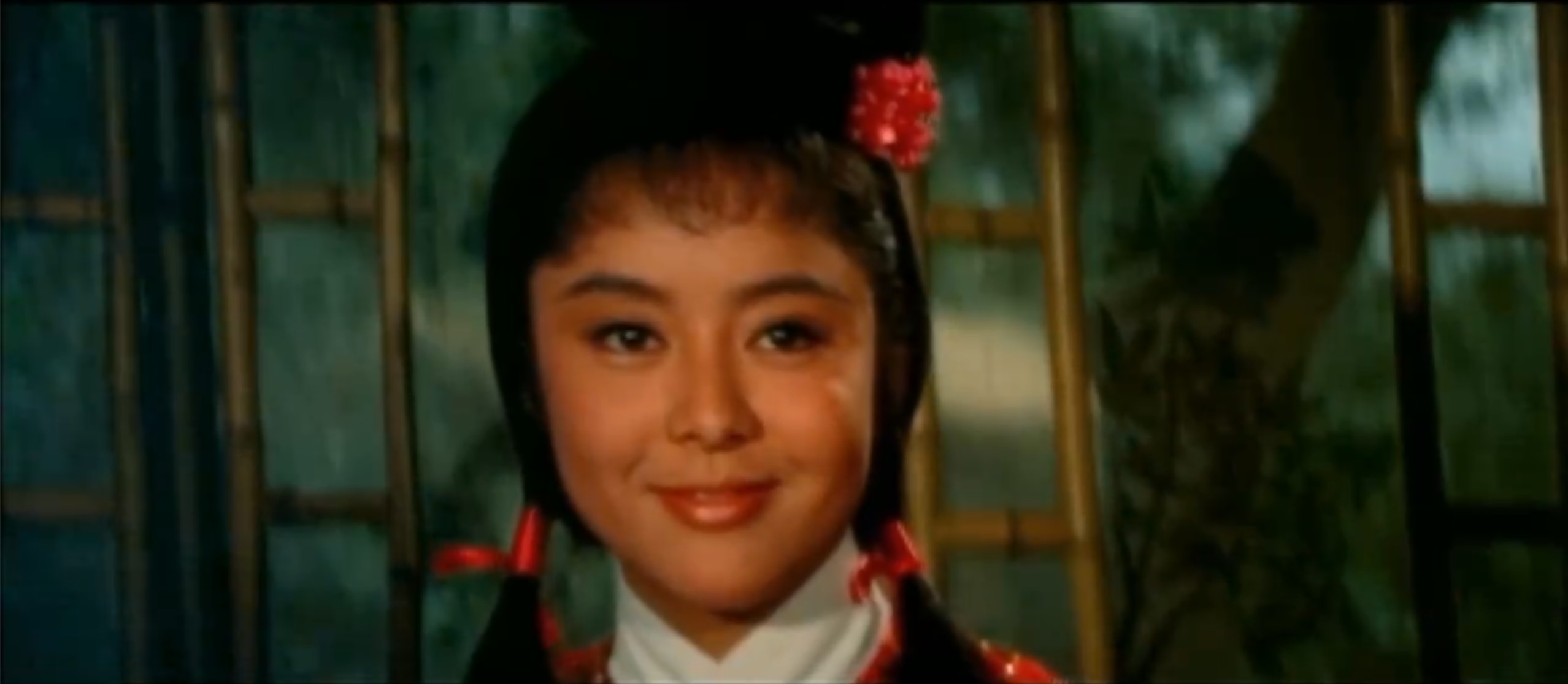 A close up picture of Margaret Hsing-Hui. Her hair is held in ponytails by red ribbons and there's a red flower in her hair.