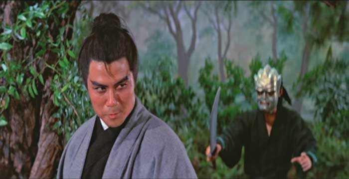 Ling Yun in a black top and grey/blue robe stands in a forest. Behind him is a man wearing a large metal mask and wielding a sword.